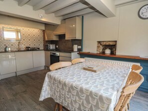 A modern kitchen with a dining area, featuring a patterned tablecloth, wooden chairs, and a stone fireplace. - Pearls Farm One (Macclesfield)