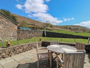A stone wall, a round wooden table with chairs, and a view of a green field with a stone wall in the background. - Pearls Farm One (Macclesfield)