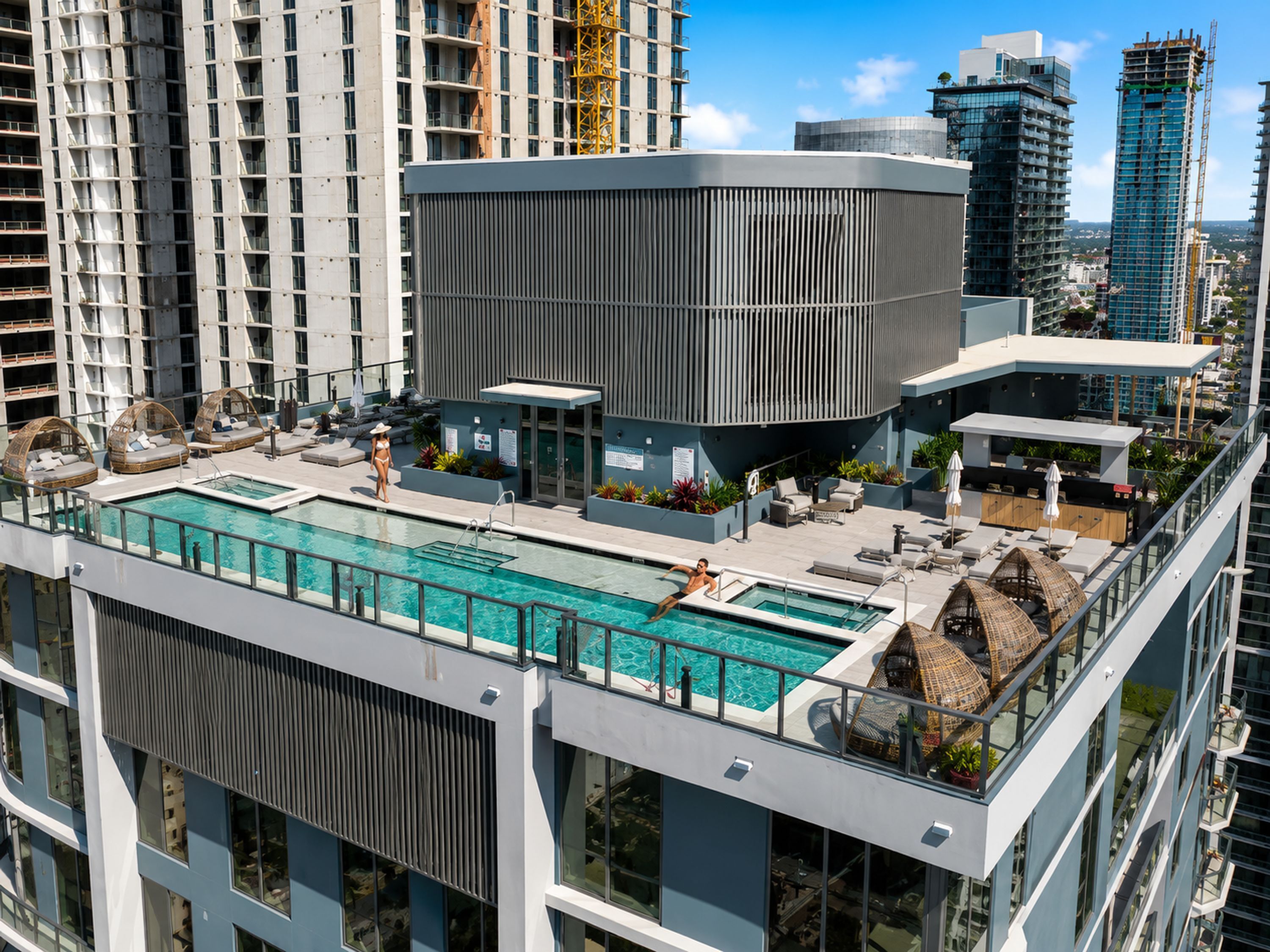 Une piscine sur le toit avec des espaces de détente, un bâtiment moderne aux lignes verticales et des immeubles de grande hauteur qui l’entourent.
