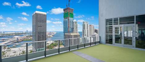 Un balcon donnant sur le panorama urbain, un plancher recouvert d’un revêtement vert et une porte d’entrée en verre.