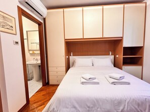 Ein Hotelzimmer mit einem Bett, einem Holzschrank, einem Badezimmer mit Waschbecken und einem gerahmten Bild an der Wand.