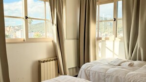 A hotel room with two beds, beige curtains, a radiator, and a window with a city view. - Dpto en pleno centro de Salta con cochera (Salta)