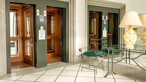 A hotel lobby with a tiled floor, wooden doors, a glass table with a lamp, and a green chair. - Dpto en pleno centro de Salta con cochera (Salta)
