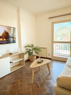 Ein Wohnzimmer mit Fernseher, einer Pflanze, einem Couchtisch aus Holz und einer Couch.