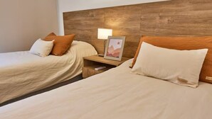 A hotel room with two beds, a wooden headboard, a bedside table with a lamp, and a framed picture.