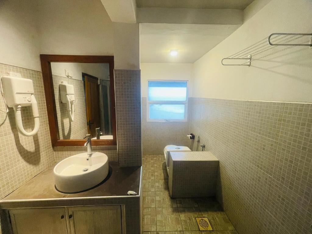 Een badkamer met een wastafel, spiegel, handdoekhouder en een raam voor natuurlijk licht.