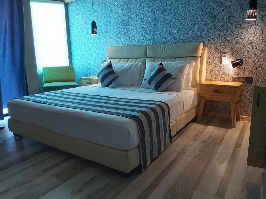 A bed with a striped blanket, a headboard, two bedside tables, and a patterned wall.