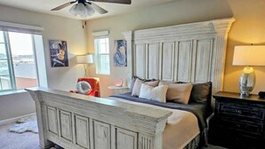Ein Schlafzimmer mit einem Bett, einem Nachttisch, einer Lampe, einem Deckenventilator und Kunstwerken an den Wänden.