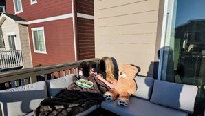 Eine Holzterrasse mit einem weißen Sofa und einem großen Teddybären.