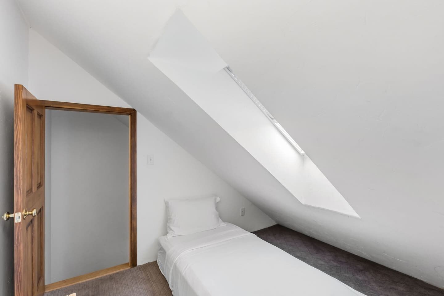 Une pièce avec un plafond en pente, un lit, une porte et une petite fenêtre.