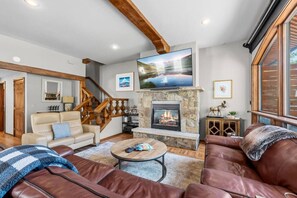 Una sala de estar acogedora con chimenea, sofás de cuero, una mesa de centro y un televisor sobre la chimenea.