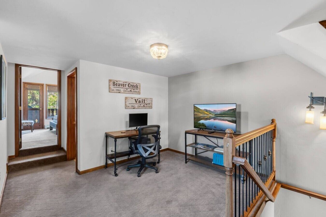 A room with a desk, chair, television, and a staircase.