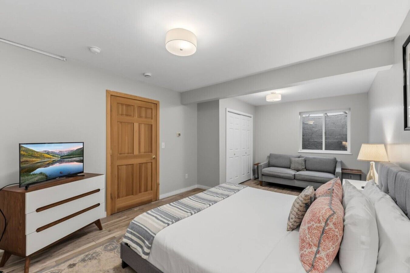 A modern bedroom with a bed, a TV, a sofa, and a window.