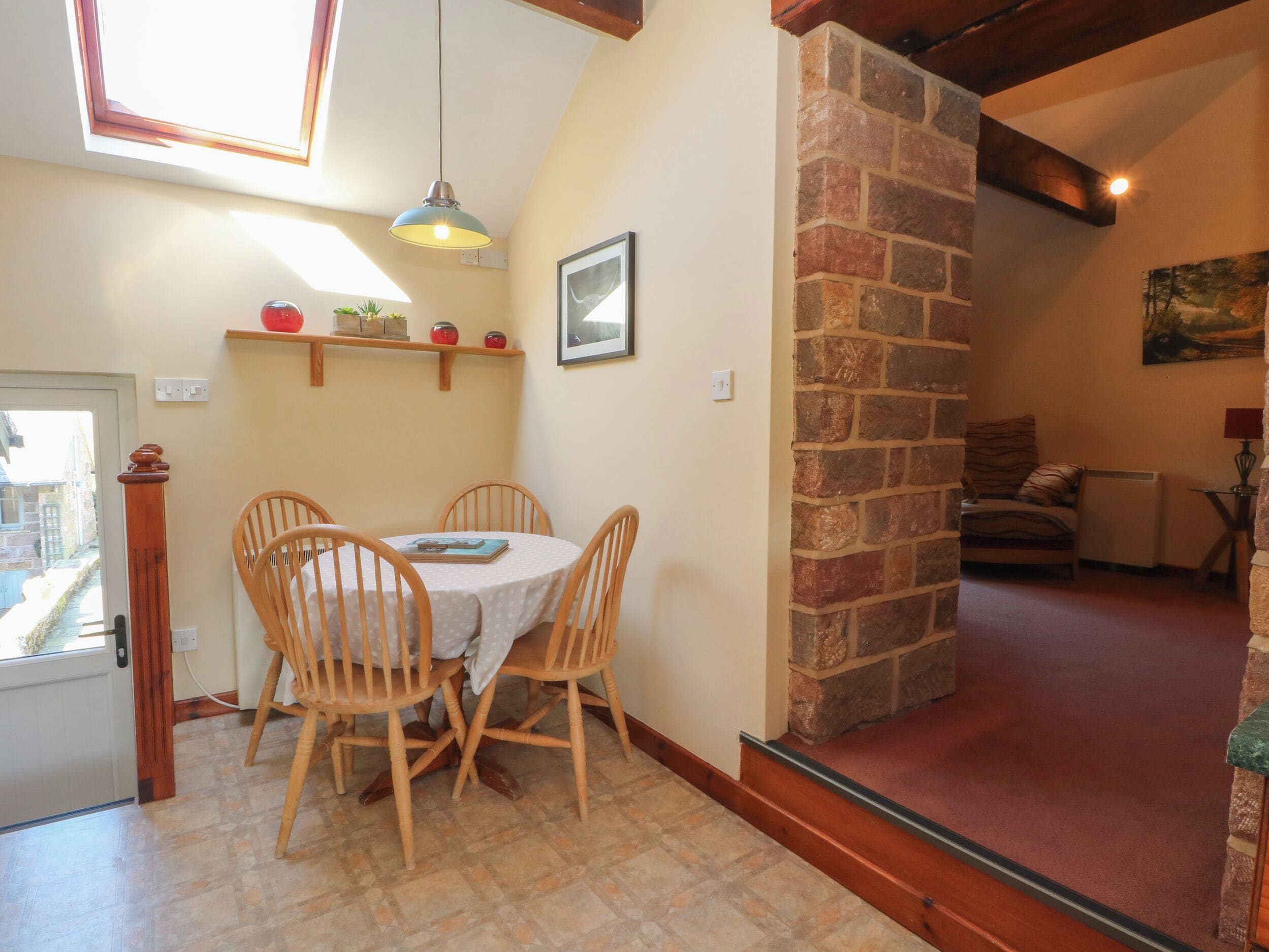 Un comedor con una mesa redonda y cuatro sillas, una lámpara colgante, una pared de piedra y un cuadro en la pared.