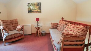 A cozy room with a bed, two chairs, a small table with a lamp, a picture on the wall, and a radiator. - Pearls Farm Two (Macclesfield)