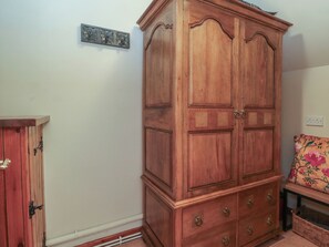 A wooden wardrobe with two doors and four drawers, a small shelf, and a decorative metal plate on the wall. - Pearls Farm Two (Macclesfield)