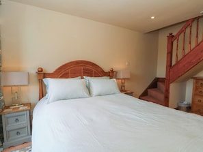 A bedroom with a wooden headboard, two bedside tables with lamps, a bed with white bedding, and a staircase with wooden railings. - Pearls Farm Two (Macclesfield)