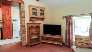 A living room with a TV, wooden cabinets, a stone wall, and a red door. - Pearls Farm Two (Macclesfield)