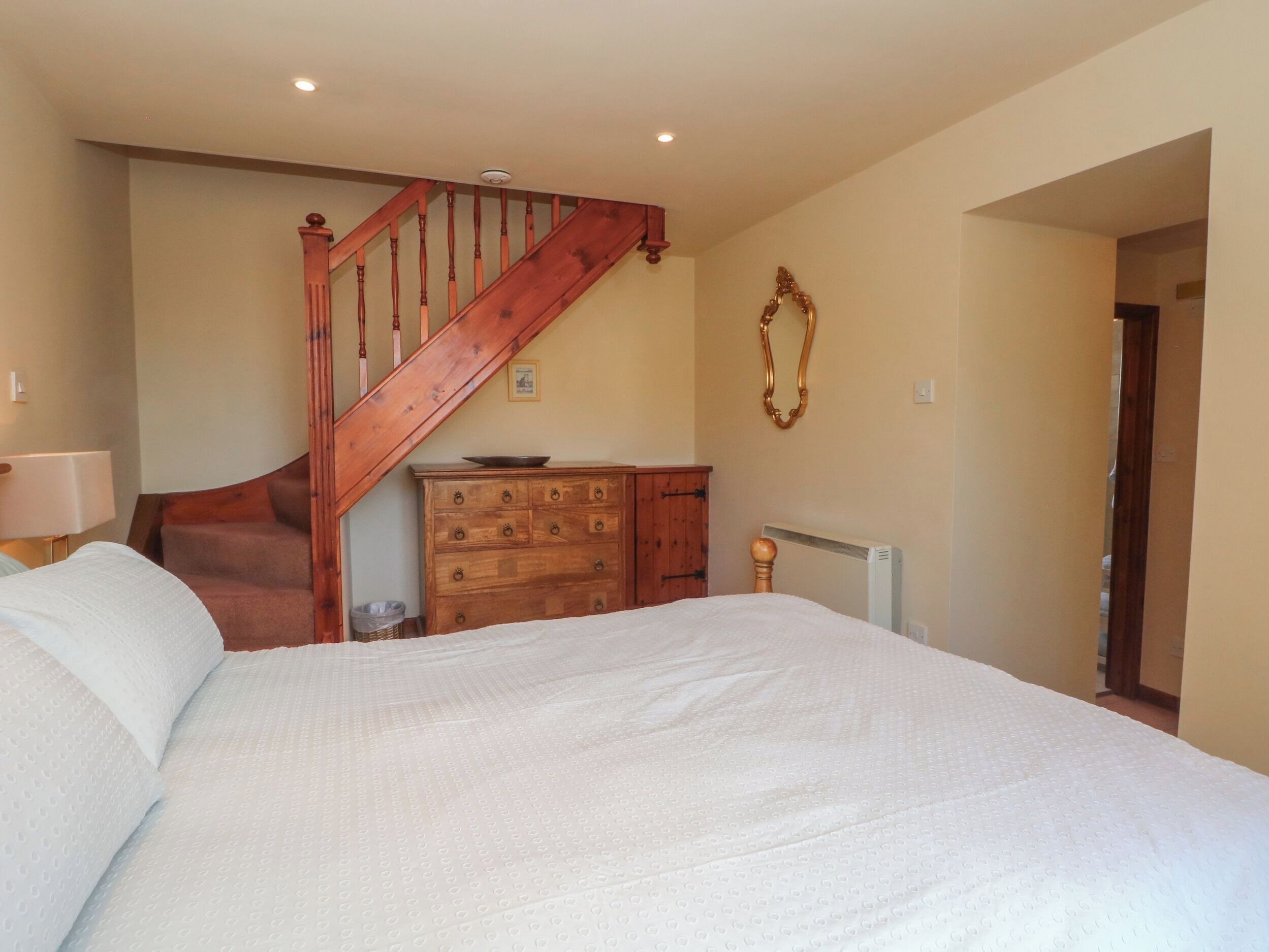 A bedroom with a wooden staircase, a dresser, a radiator, and a bed.