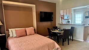 Makuuhuoneessa on sänky, televisio, ruokailutila, jossa on tuoleja ja pöytä, sekä pieni keittiönurkkaus.