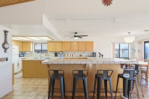 A kitchen with wooden cabinets, a large island with stools, a ceiling fan, and a view of the city.