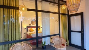 Una habitación con una cama, dos sillones de mimbre, una mesita y una lámpara colgante.
