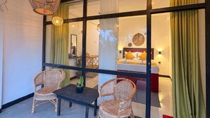 Una habitación con separador de vidrio, sillas de mimbre, una mesita y lámparas colgantes.
