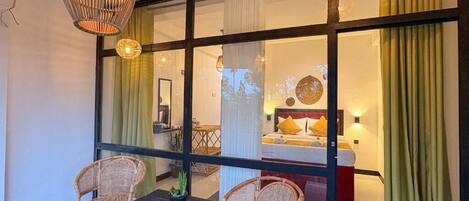 Quarto com divisória de vidro, cadeiras de vime, uma mesinha e luminárias pendentes.
