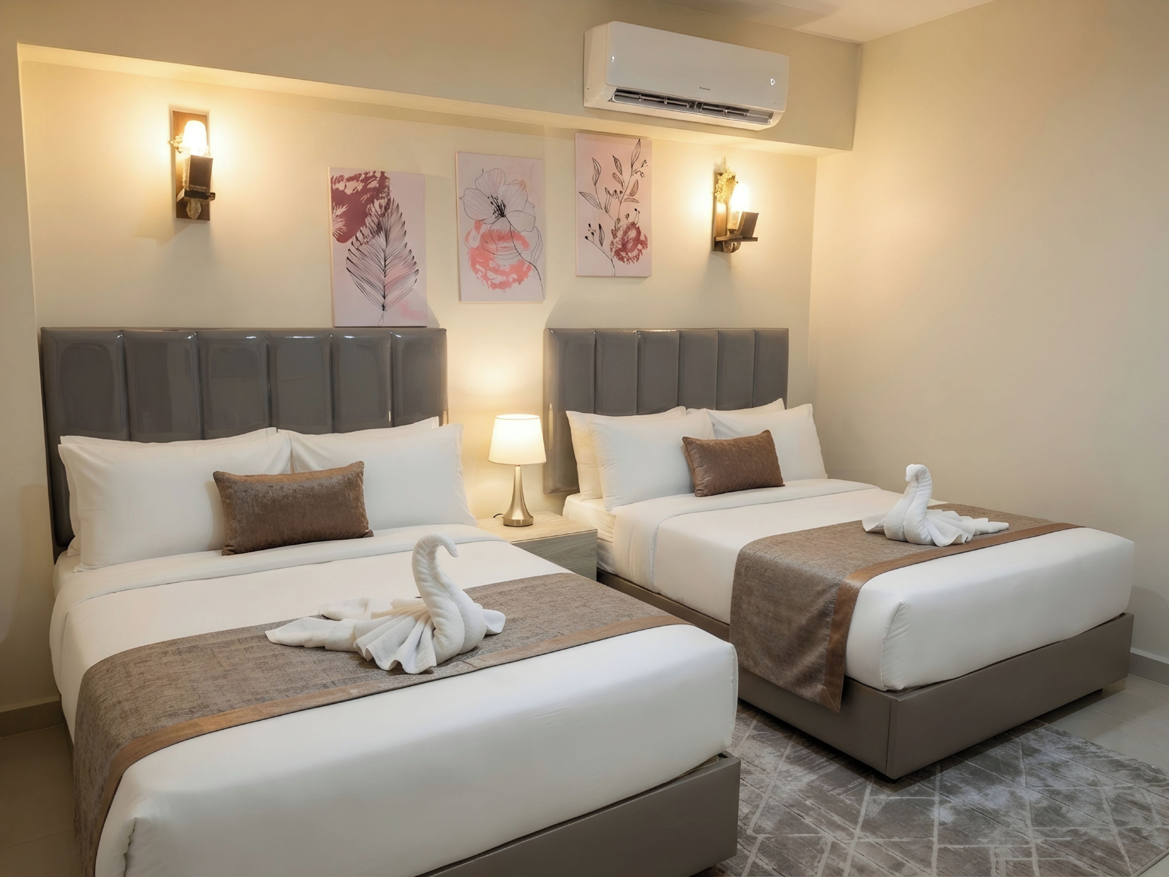 A hotel room with two beds, each with a headboard, bedside tables, and wall-mounted lamps.