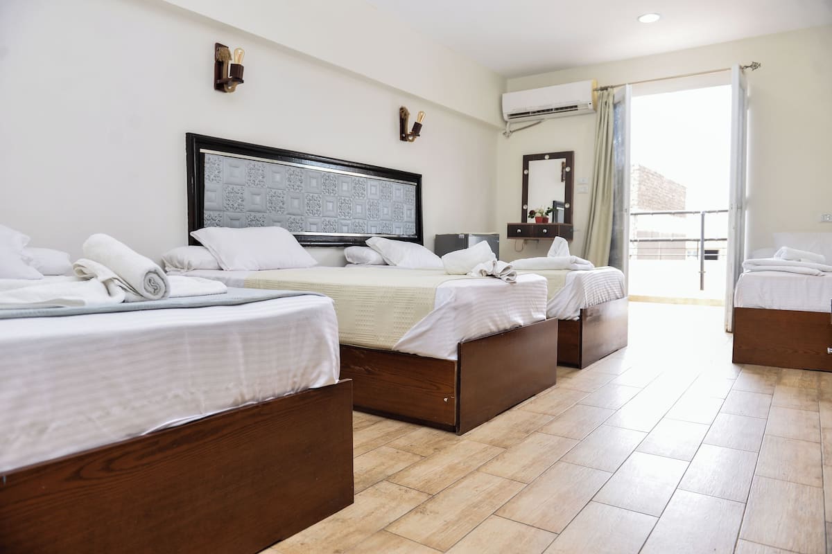 Quarto de hotel com três camas, um espelho grande, ar condicionado e vista para o exterior.