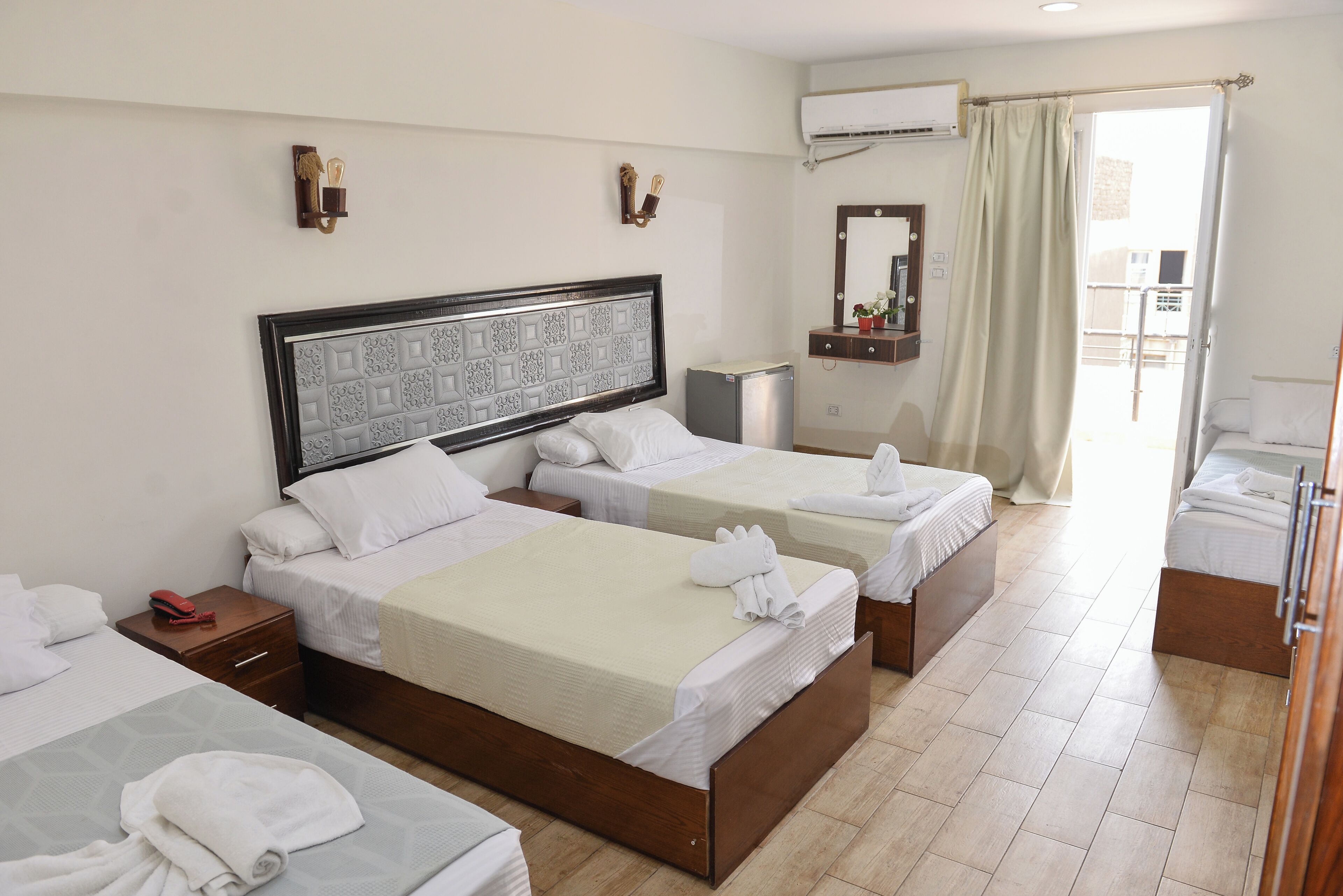 A hotel room with three beds, a small desk, a mirror, and an air conditioning unit.
