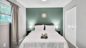 Quarto de hotel com cama, duas mesas de cabeceira, um relógio na parede e uma janela com cortinas.