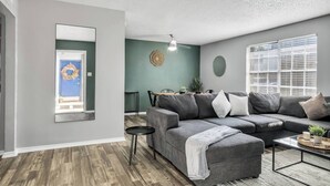 Ein modernes Wohnzimmer mit einem grauen Sofa, einem Couchtisch und einem Essbereich mit Tisch und Stühlen.