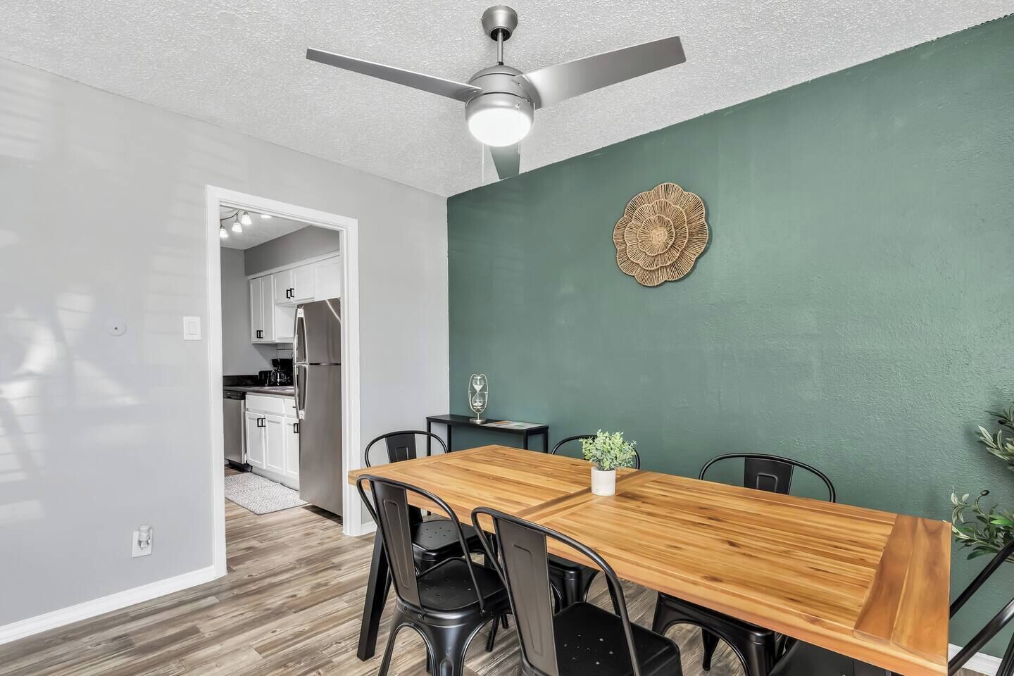 A dining area with a wooden table, black chairs, a ceiling fan, and a green accent wall.