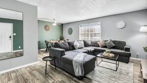 Ein modernes Wohnzimmer mit einer Eckcouch, einem runden Couchtisch und einem Essbereich mit Tisch und Stühlen.