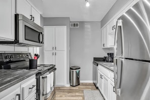 Una cocina moderna con electrodomésticos de acero inoxidable, armarios blancos y encimera negra.