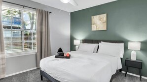 Ein Hotelzimmer mit einem Bett, zwei Nachttischlampen, einem Deckenventilator, einem Fenster mit Vorhängen und einem Bild an der Wand.