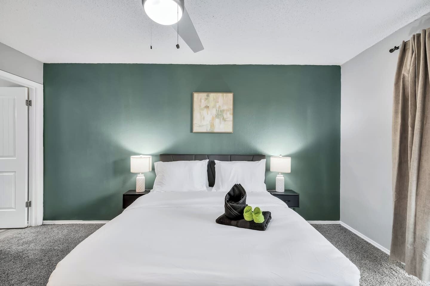 Une chambre d’hôtel avec un lit, deux tables de chevet avec des lampes, un ventilateur de plafond, une porte et un mur vert.