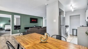 A modern living space with a dining area, a sofa, a TV mounted on the wall, and a kitchen area.