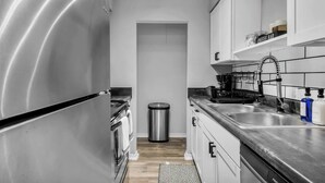 A modern kitchen with stainless steel appliances, a trash bin, and a sink with soap dispensers.