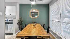 A dining area with a wooden table, black chairs, a ceiling fan, and a green wall with a mirror.