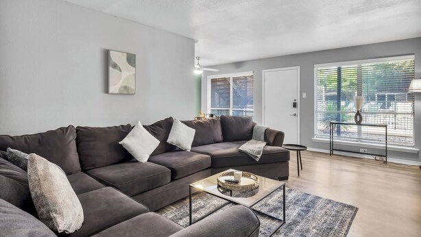 A modern living room with a sectional sofa, a coffee table, and a view through large windows.