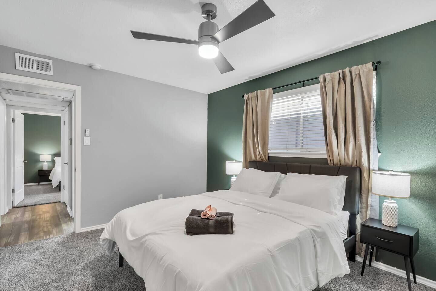 A bedroom with a bed, a ceiling fan, a window with curtains, a nightstand, and a lamp.