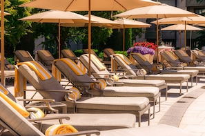 Une rangée de chaises longues dotées de coussins à rayures, disposées en ligne sous de grands parasols.