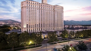 A large, multi-story hotel with a prominent tower, surrounded by trees and a road with moving vehicles.