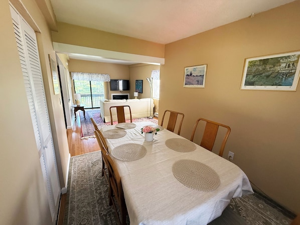 A dining area with a table set for four, a sofa, a TV, and a window with blinds.