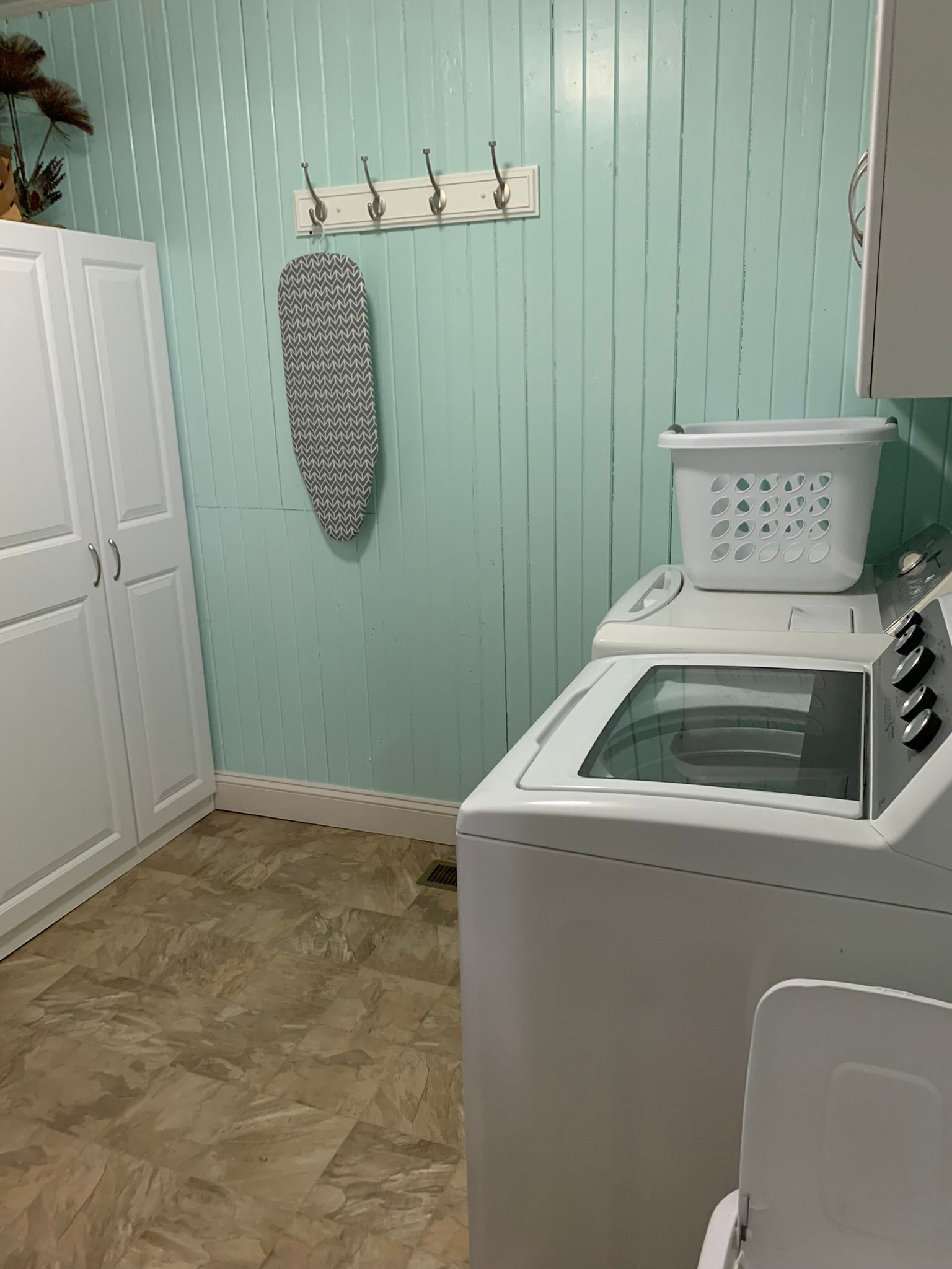 Une buanderie équipée d’un lave-linge, d’un étendoir et d’un panier à linge fixé au mur.