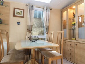 Un comedor con una mesa de vidrio, sillas de madera, una ventana con cortinas y un mueble de madera con puertas de cristal.