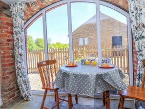 A dining area with a table set for two, a wooden chair, and a view of a brick building through large windows. - The Granary (York)