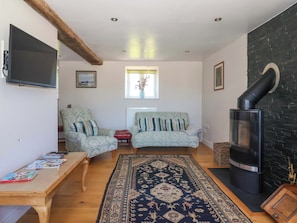 Una sala de estar con dos sillones con diseños, un sofá, una mesa de centro de madera con revistas, una alfombra grande, una chimenea y un televisor montado en la pared.